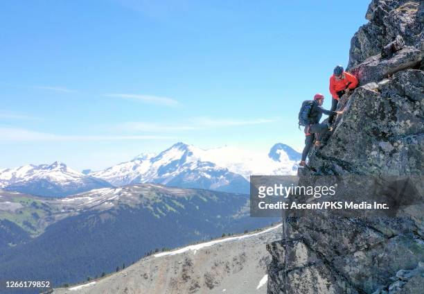 mountaineers ascend rock cliff, above snowcapped mountains - messa in sicurezza foto e immagini stock
