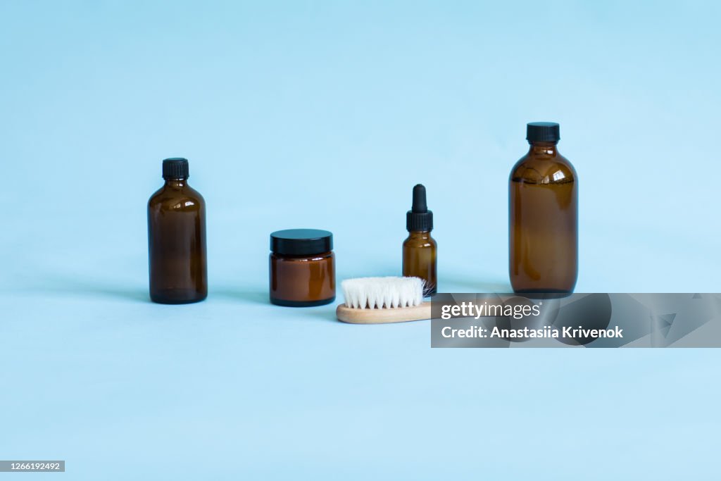 Dark amber glass cosmetic bottles on blue studio background. Set of accessories for hygiene. Beauty blogging, salon treatment concept, minimalism brand packaging mock up.