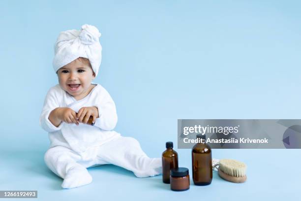 cute baby wearing bath clothes playing with cosmetics bottle on blue background. adorable child advertise set of baby accessories for hygiene. baby bath time concept. - baby background stockfoto's en -beelden