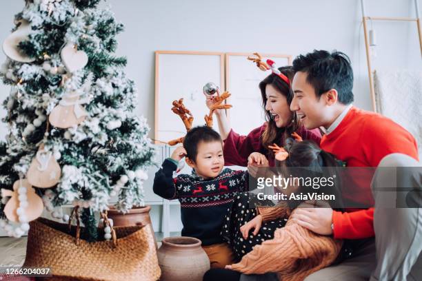 christmas lifestyle theme. happy asian family decorating christmas tree together in the living room at home. they are putting on various baubles and ornaments and enjoying their holiday - tradition stock pictures, royalty-free photos & images