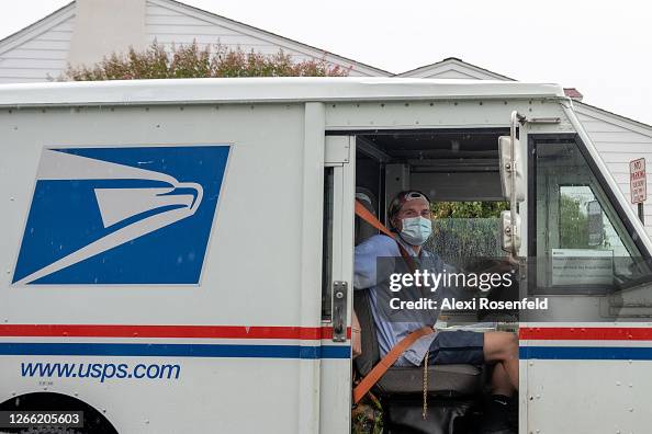 Mail Driver A USPS mail worker wearing a mask poses in his truck while it rains ...