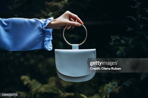 a woman's hand holds handbag in her hand on a dark background - blue purse stock-fotos und bilder