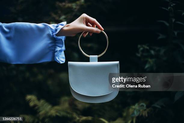 a woman's hand holds handbag in her hand on a dark background - blue purse stock pictures, royalty-free photos & images