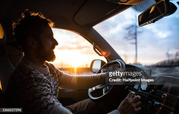 side view of mature man driving car at sunset in winter. - zwielicht stock-fotos und bilder