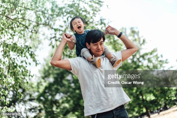 father carrying daughter on shoulder at the park - carrying on shoulders stock pictures, royalty-free photos & images