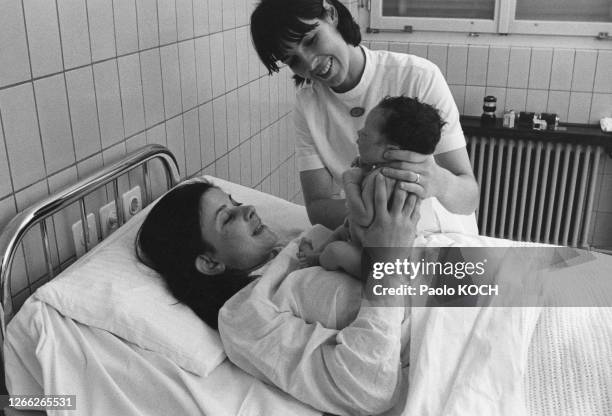 Sage-femme présentant un nouveau-né à sa maman dans une maternité en Suisse, circa 1970.