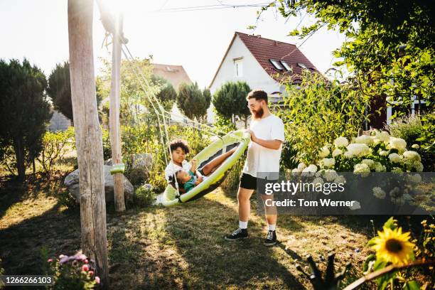 dad pushing kids on swing in back garden together - family garden play area stock pictures, royalty-free photos & images