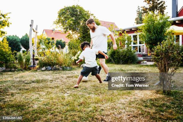 father playing football with his young young son in back garden - fussball rasen stock-fotos und bilder