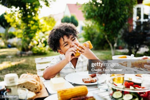 young boy eating barbecued corn on the cob - bbq corn foto e immagini stock