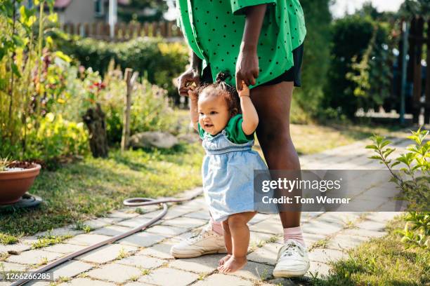 mother holding baby's hands while walking her - first step stock-fotos und bilder