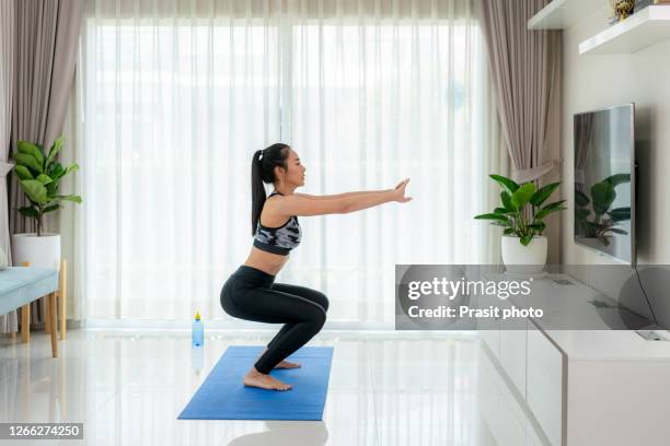 asian fit young woman training at home. beautiful female athlete working out for wellbeing in domestic gym, training legs muscles doing side to side squats in living room. - squatting position - fotografias e filmes do acervo