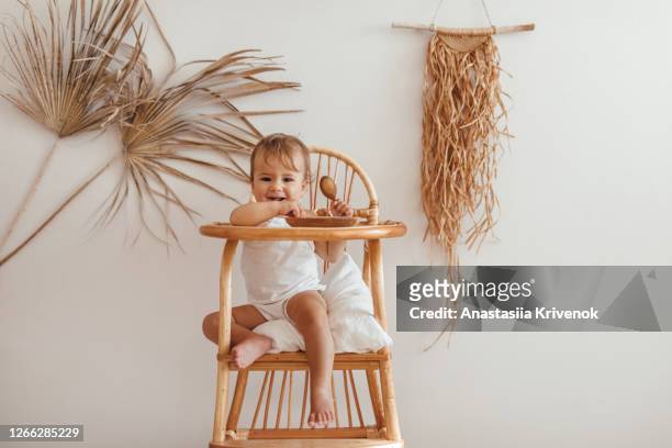 adorable baby girl sitting on ecological wooden children's dining chair. baby room in natural and organic materials. zero waste concept. - craft food fotografías e imágenes de stock