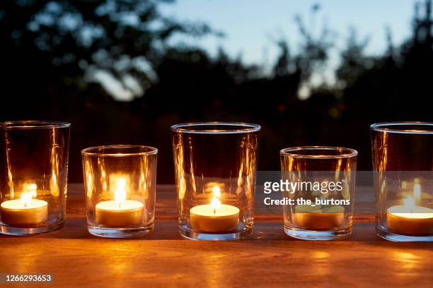 lit tea light candles in glasses in a row on table in garden during sunset - lampion verlichting stockfoto's en -beelden