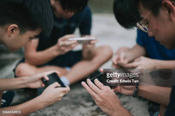 en asiatisk kinesisk grupp av tonårspojkar spelar mobilspel i basketplanen efter skolan med hjälp av telefon generation z - friendly match bildbanksfoton och bilder