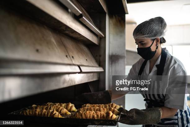 bäckerin entfernt frisches brot mit gesichtsmaske aus dem ofen - savoury food stock-fotos und bilder