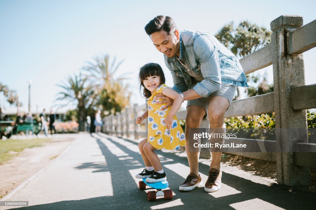 Vater hilft jungen Tochter Reiten Skateboard