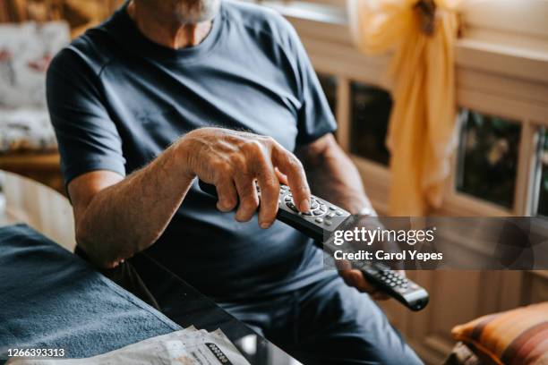 closeup image of a senior man with tv remote crontrol watching tv at home - tv-sign-off stock pictures, royalty-free photos & images