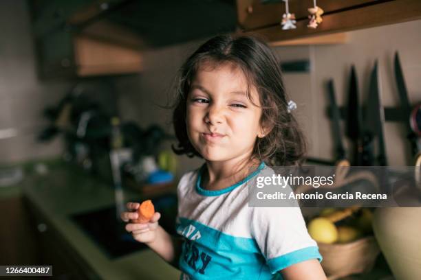 pretty 4 years girl eating carrot in kitchen, sitting on her kitchen counter - funny vegetable stock-fotos und bilder