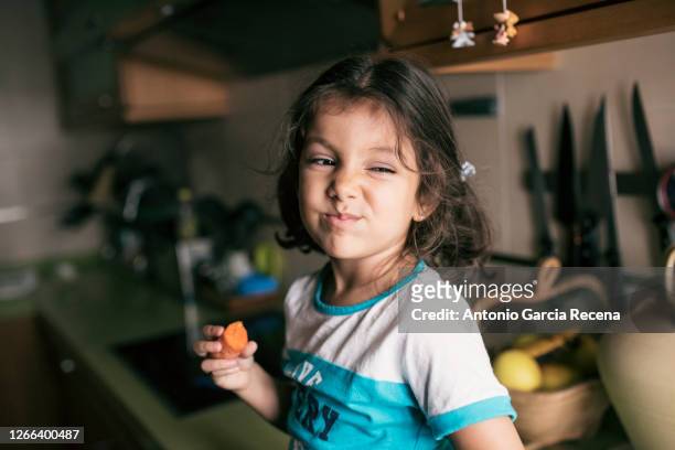 pretty 4 years girl eating carrot in kitchen, sitting on her kitchen counter - 4 5 years foto e immagini stock