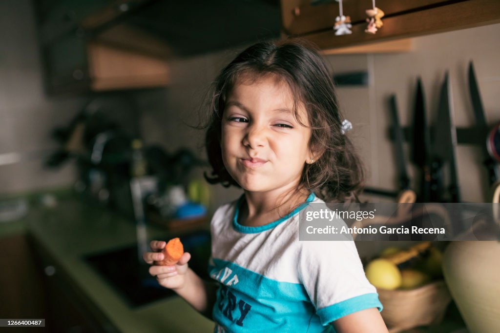 Pretty 4 years girl eating carrot in kitchen, sitting on her kitchen counter