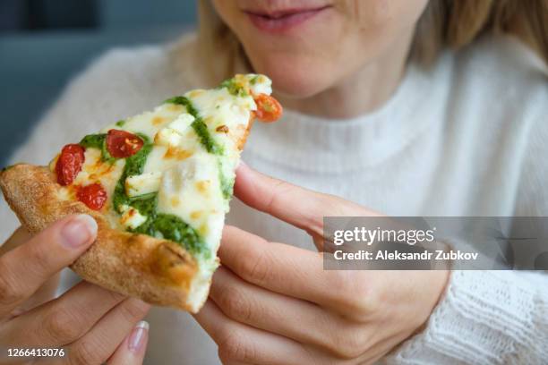 a slice of italian pizza margarita or pesto with cheese in the hands of a girl. a woman takes a slice of pizza and eats it, in a cafe or pizzeria. vegetarian food. fast food. - eating pesto stock pictures, royalty-free photos & images