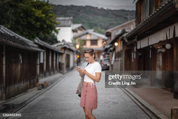 young woman checking mobile phone on the empty street in kyoto - japan tourist stock pictures, royalty-free photos & images