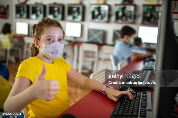 schoolgirl with protective face mask showing thumb up during computer class at private school - male feet on face stock pictures, royalty-free photos & images