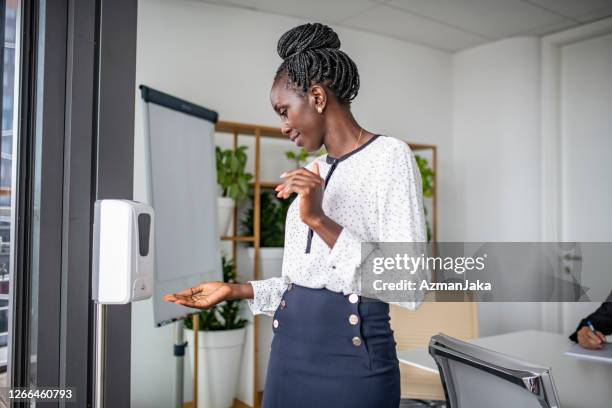 african businesswoman using hand sanitizer in office - hand sanitizer stock pictures, royalty-free photos & images