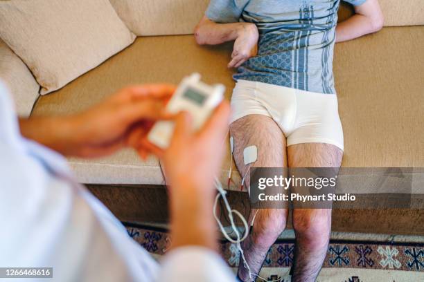 physiotherapist applying electro stimulation in physical therapy to a young man leg - electro acupuncture stock pictures, royalty-free photos & images