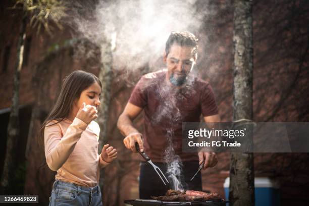 father cutting a slice of meat to his daughter during a barbecue - brazilian culture stock pictures, royalty-free photos & images
