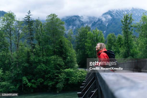 junge backpackerin wandert über brücke im wald - red coat stock-fotos und bilder