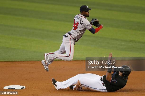 Adeiny Hechavarria of the Atlanta Braves turns a double play over the sliding Jesus Aguilar of the Miami Marlins during the first inning at Marlins...