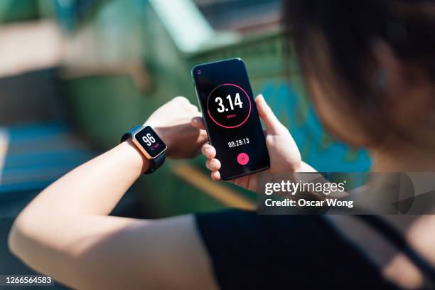 young woman using fitness app on smart phone and smart watch for tracking workout - egg timer stock-fotos und bilder