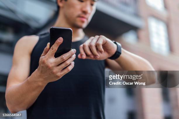young man using fitness app on smart phone and smart watch for tracking workout - checking sports stock pictures, royalty-free photos & images