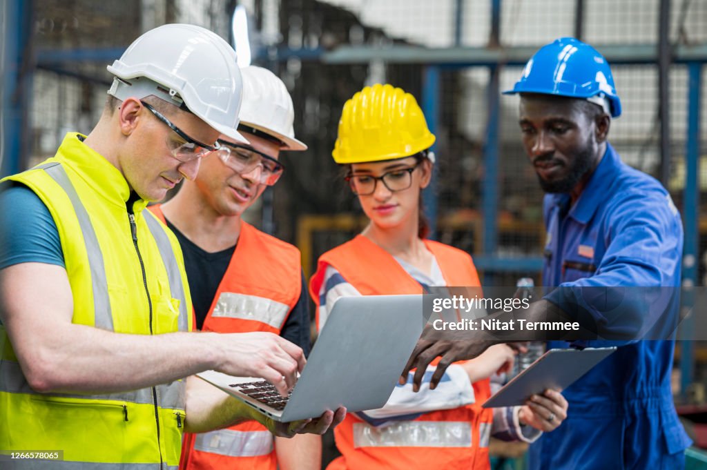 Multi-ethnic workers having meeting. Colleague brainstorming in front of production line at a heavy industry having discussion with manual worker and production manager.