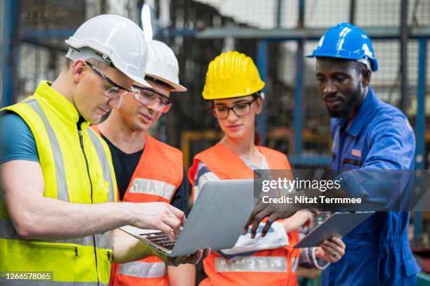 multi-ethnic workers having meeting. colleague brainstorming in front of production line at a heavy industry having discussion with manual worker and production manager. - industria pesada fotografías e imágenes de stock