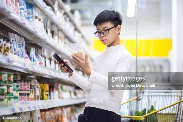 chinesische teenager lesen ernährungsfakten. er kauft artikel folgen sie der liste in seinem mobilen gerät. - teenager boy shopping stock-fotos und bilder