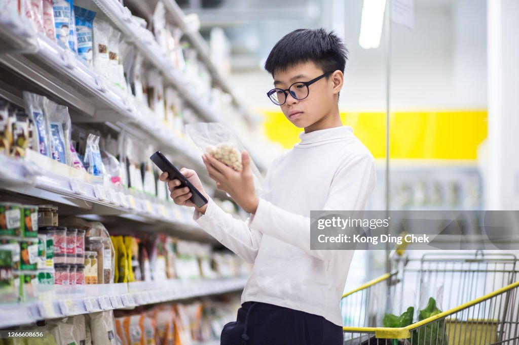 Chinese Teenager reading nutrition facts. He is buying item follow the list in his mobile device.