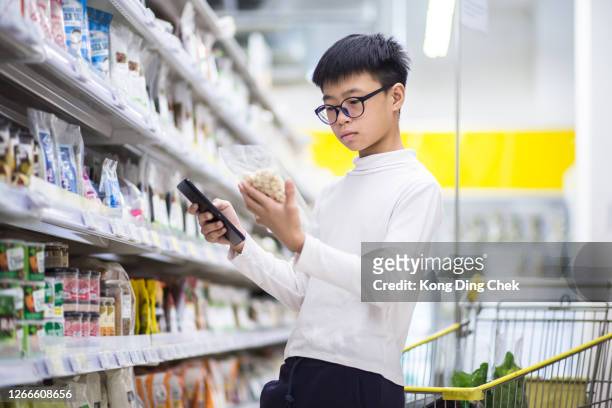 chinese teenager reading nutrition facts. he is buying item follow the list in his mobile device. - teenager boy shopping stock pictures, royalty-free photos & images