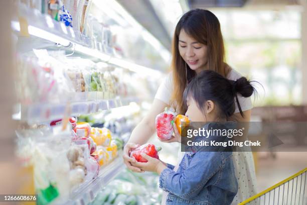 chinesische frauen mit tochter entscheiden sich für frisches gemüse im lebensmittelgeschäft. - asian family shopping stock-fotos und bilder
