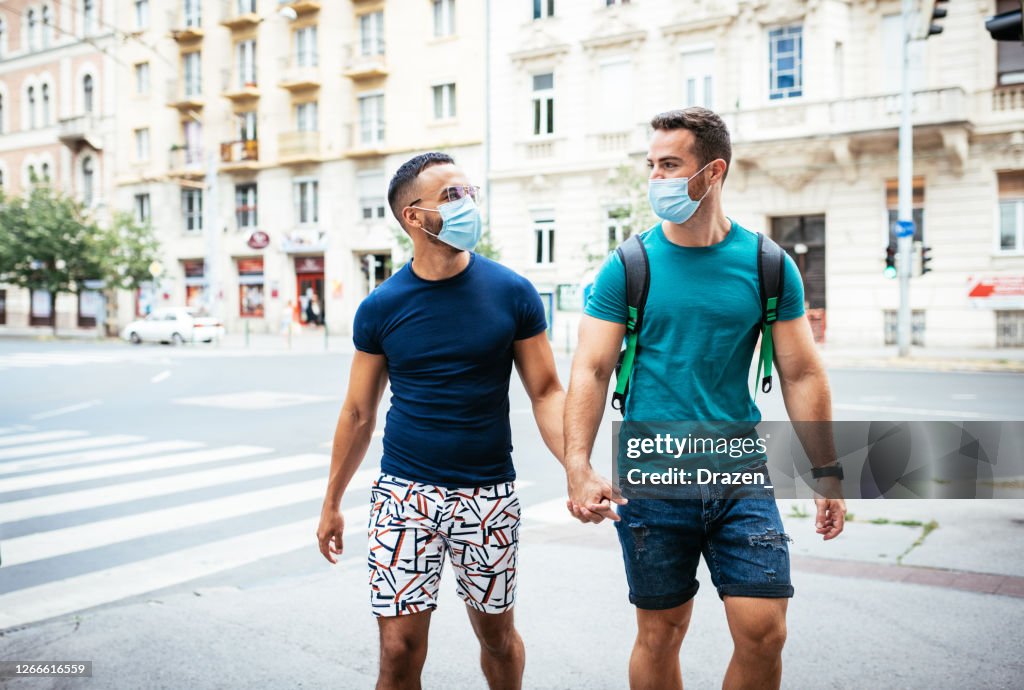 Gay couple with face masks outdoors in the city during lockdown