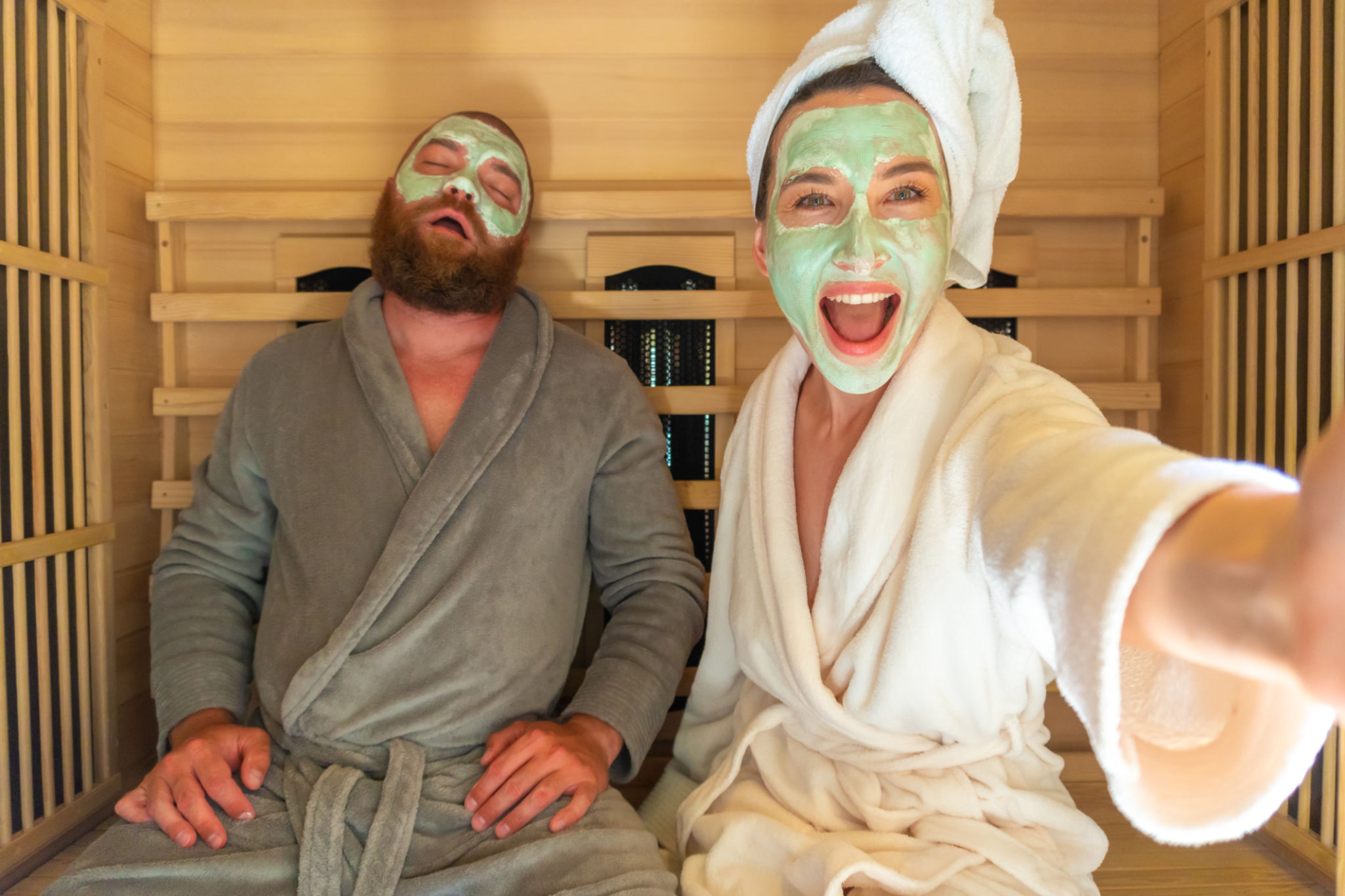 A young funny couple having relax SPA day in sauna, a woman making selfie with beauty mask while her boyfriend is asleep. A young funny couple having relax SPA day in sauna, a woman making selfie with beauty mask while her boyfriend is asleep.