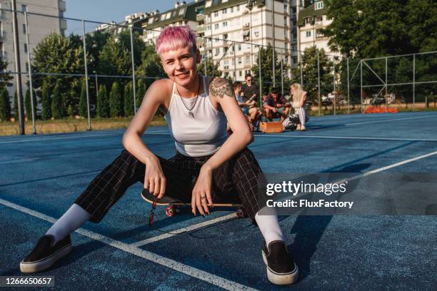 skateboarding girl with pink hair sitting in front of a group of friends on a sports court - womens free skate imagens e fotografias de stock