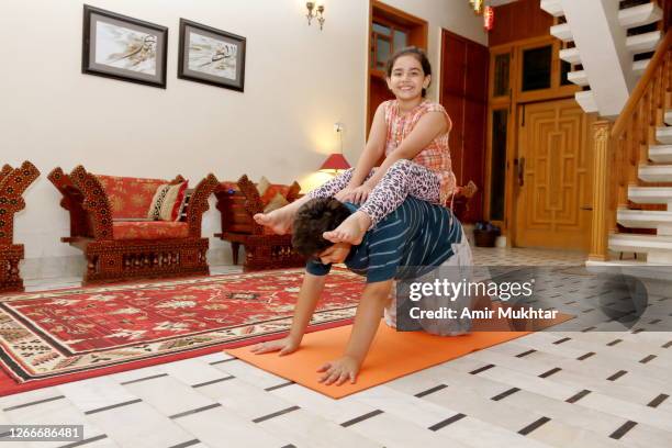 a boy in pushups position and a little girl sitting on his back in side the domestic room on exercise mat. - punjab pakistan stockfoto's en -beelden