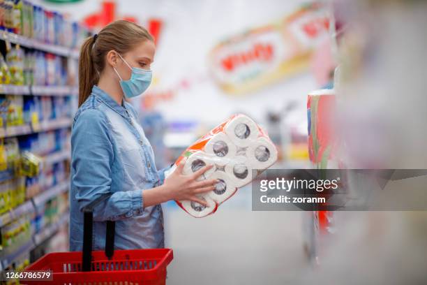 young woman with face mask holding and looking at toilet paper pack in store - buying toilet paper stock pictures, royalty-free photos & images
