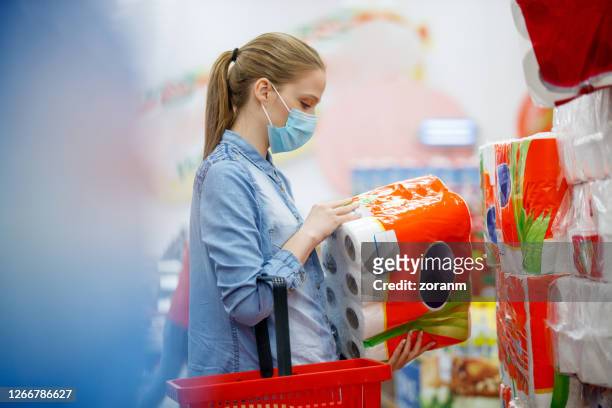 woman in face mask holding and looking at large pack of toilet paper - buying toilet paper stock pictures, royalty-free photos & images