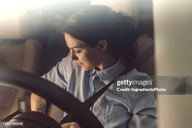 young woman is fastening her seat belt in the car. - fasten stock pictures, royalty-free photos & images