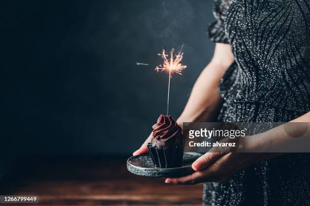 woman holding birthday cupcake with firework candle - anniversary stock pictures, royalty-free photos & images