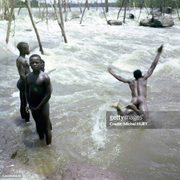 Enfants se baignant devant une pêcherie enya sur le fleuve Congo, dans la province Orientale, circa 1960, République démocratique du Congo.