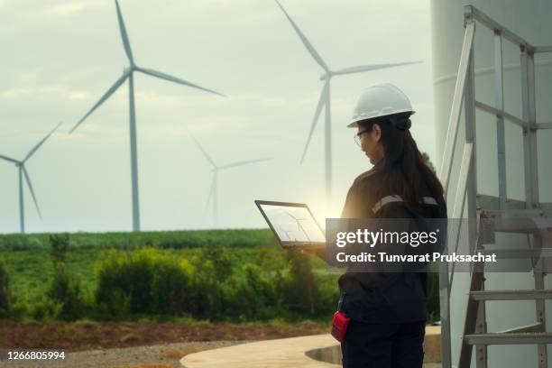 female engineer wearing hard hat standing with digital tablet against wind turbine. - ecosystem stock pictures, royalty-free photos & images